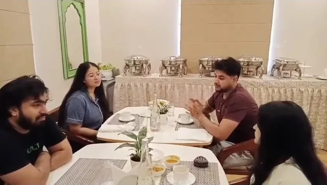 Video still: four guests talking at a table in the dining hall